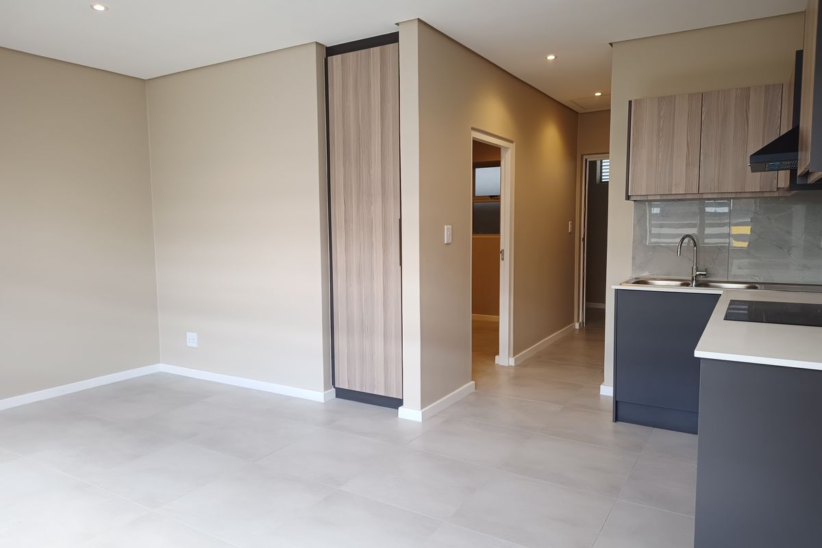 Modern open-plan living area featuring a sleek kitchen with built-in cabinetry, stone countertops, integrated hob, and neutral tiled flooring throughout.