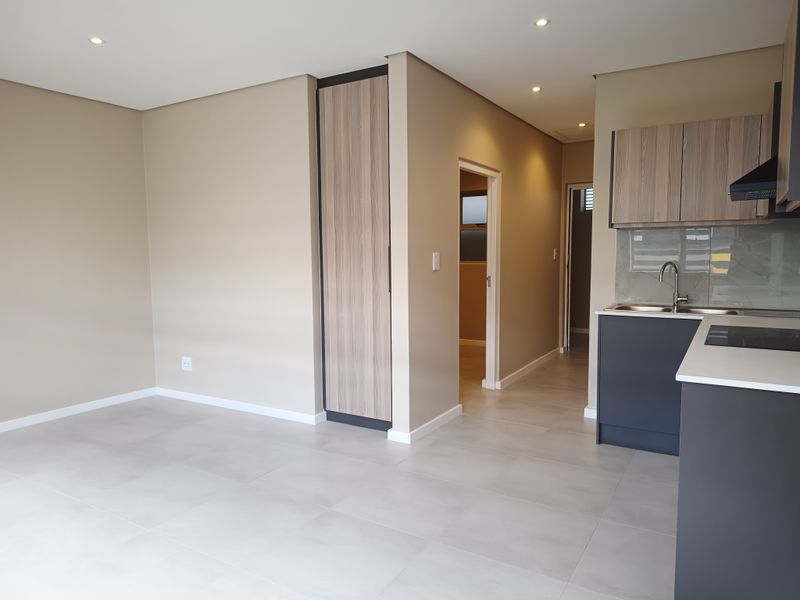 Modern open-plan living area featuring a sleek kitchen with built-in cabinetry, stone countertops, integrated hob, and neutral tiled flooring throughout.