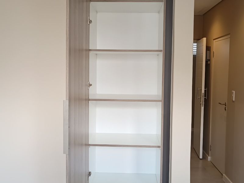A clean, modern hallway featuring a tall built-in storage cupboard with shelving and neutral tiled flooring.
