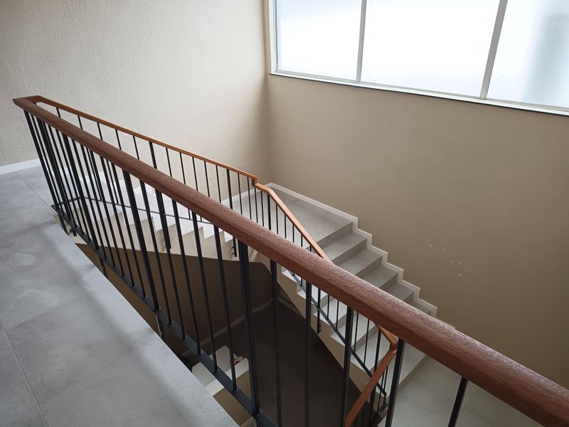 A bright, modern staircase featuring a sleek metal balustrade with a wooden handrail, tiled steps, and a large window providing natural light.