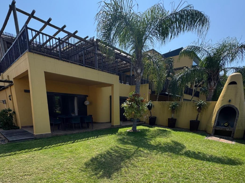 A spacious rear garden featuring a covered patio with a wooden pergola, a well-maintained lawn, and a unique built-in outdoor fireplace.
