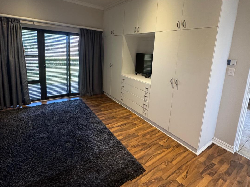 A well-maintained bedroom featuring extensive built-in cabinetry, warm laminate flooring, and a sliding glass door providing natural light and garden access.