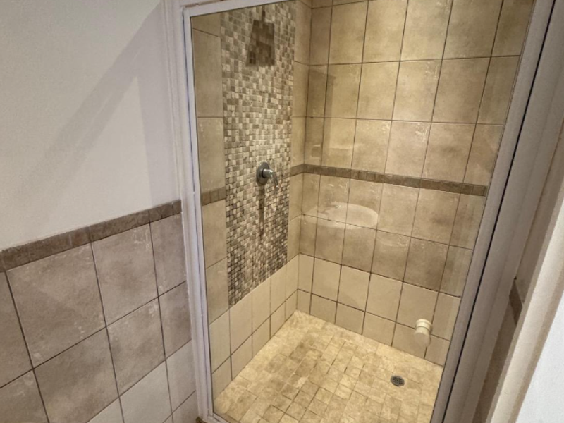 A functional shower stall featuring neutral-toned ceramic wall tiles with a decorative mosaic accent strip and a white-framed glass enclosure.