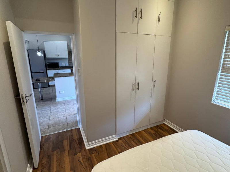 A well-maintained bedroom featuring laminate flooring, built-in cupboards, and a view through the doorway into the adjacent kitchen area.