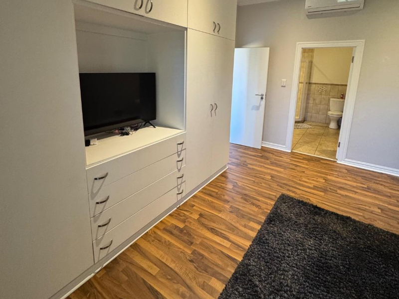 Spacious bedroom featuring extensive built-in cabinetry, laminate flooring, and a wall-mounted air conditioning unit, with direct access to an en-suite bathroom.