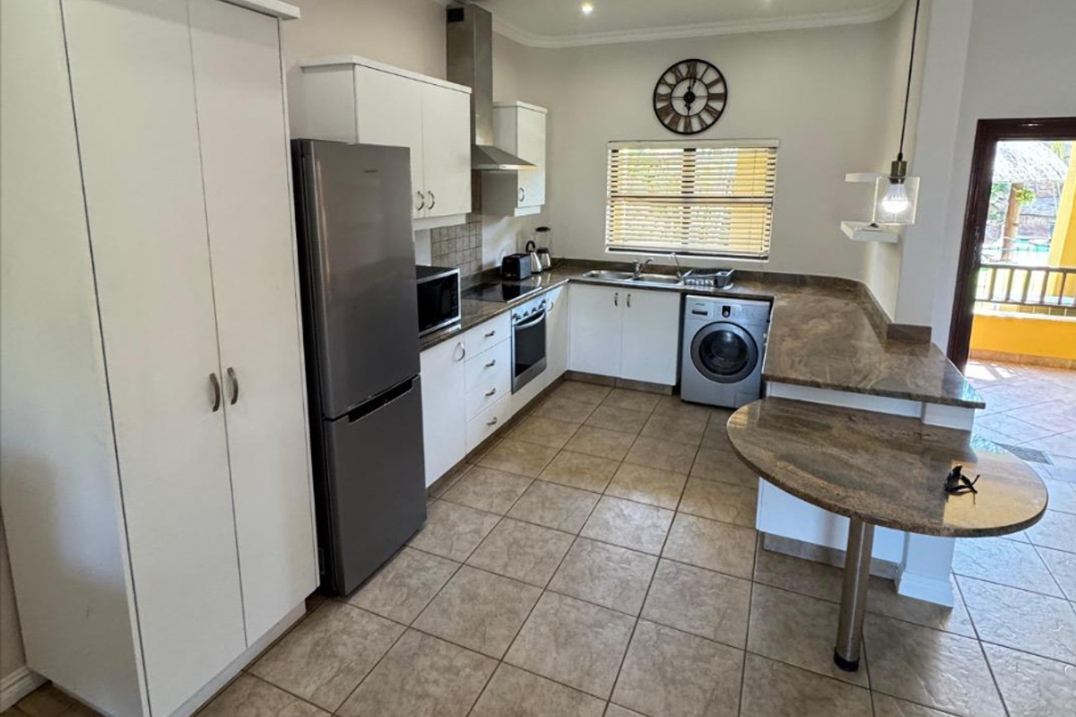 A functional kitchen featuring stone countertops, built-in cabinetry, a breakfast bar, and integrated appliances, with direct access to an outdoor balcony area.