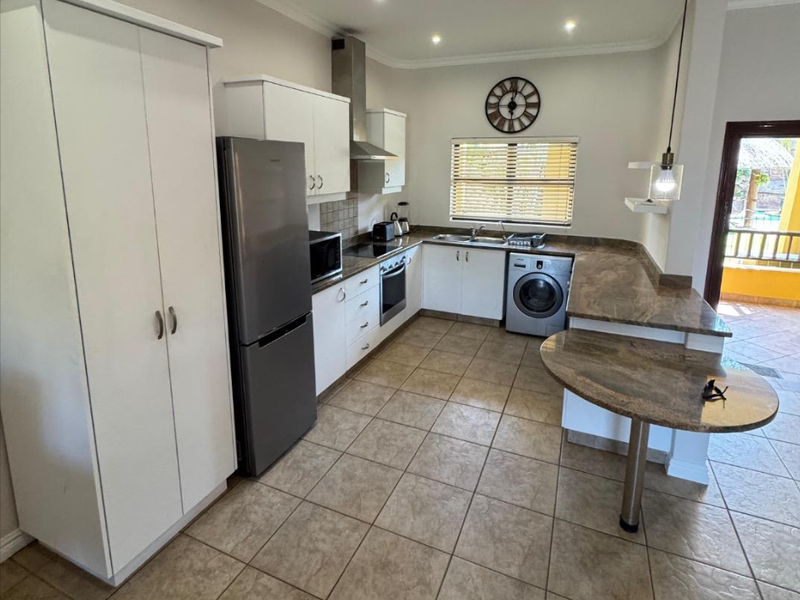 A functional kitchen featuring stone countertops, built-in cabinetry, a breakfast bar, and integrated appliances, with direct access to an outdoor balcony area.