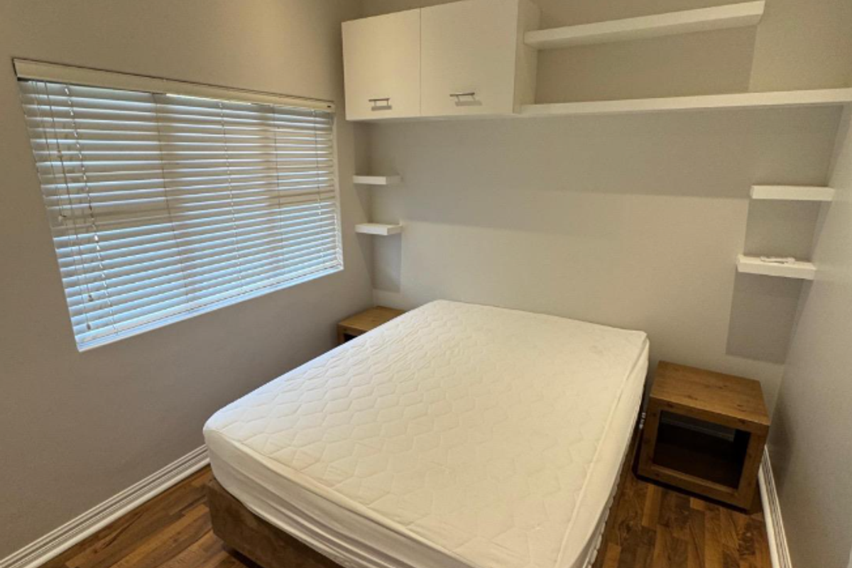 A well-maintained bedroom featuring laminate flooring, built-in overhead cabinetry, floating shelving, and venetian blinds.