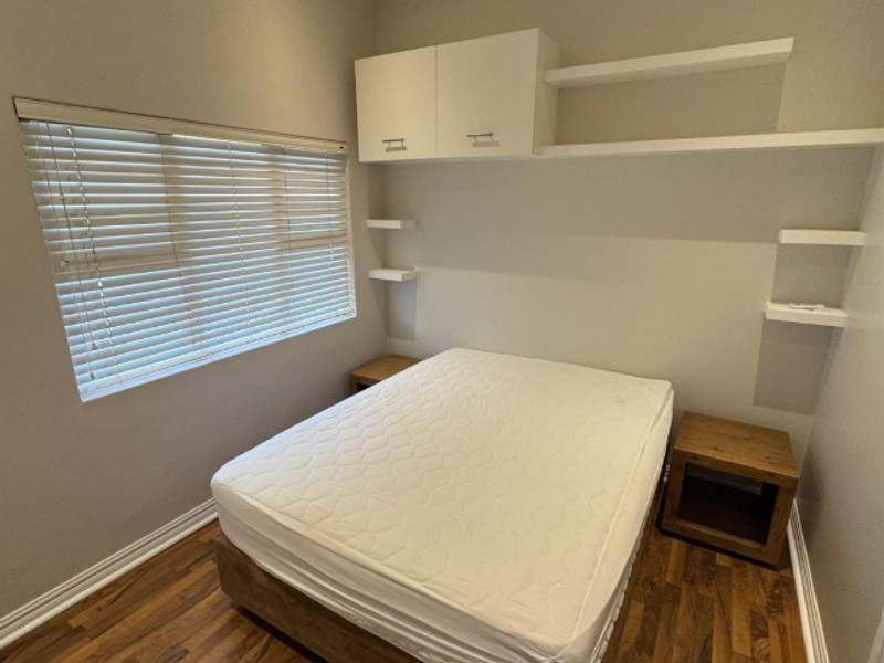 A well-maintained bedroom featuring laminate flooring, built-in overhead cabinetry, floating shelving, and venetian blinds.