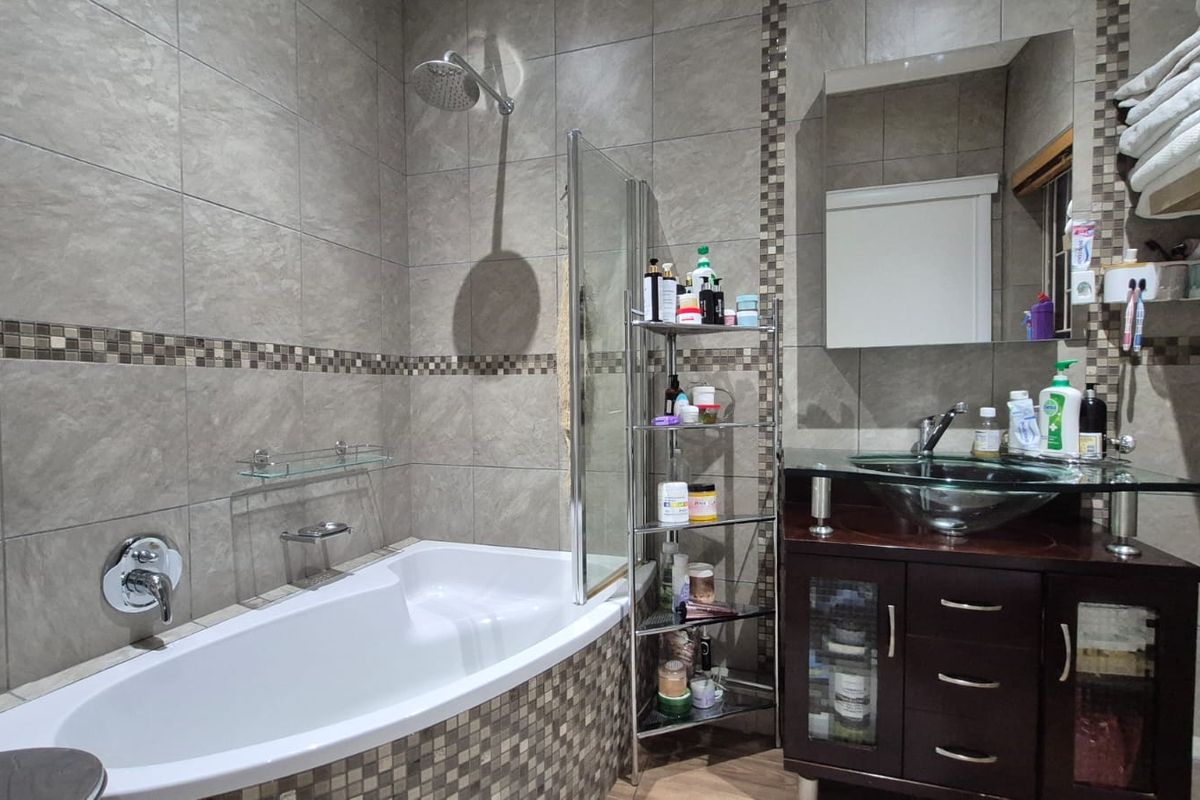 A modern bathroom featuring a built-in bathtub with a glass shower screen, a dark wood vanity cabinet with a glass vessel sink, and tiled walls.