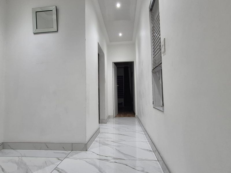 A bright, empty hallway featuring modern marble-look floor tiles, recessed ceiling lighting, and neutral white walls.