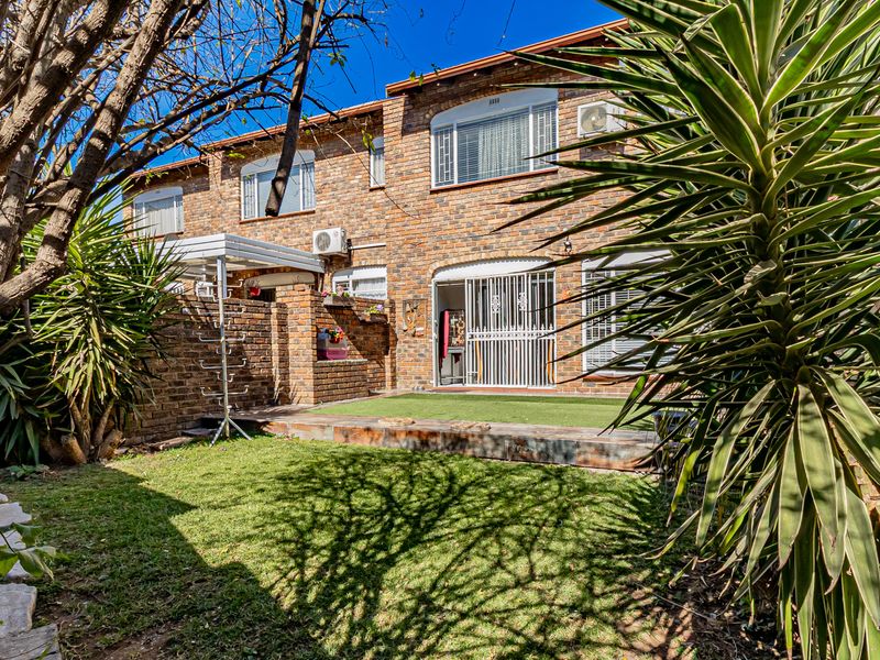 A private rear garden featuring a face brick facade, paved patio area, and artificial lawn, providing a low-maintenance outdoor space for the apartment.