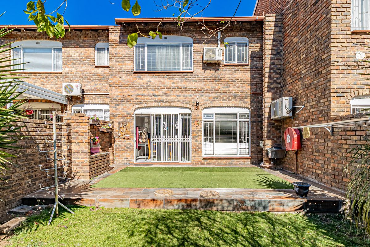 Rear exterior view of a face brick apartment featuring a tiled patio area, artificial lawn, and secure sliding door access.