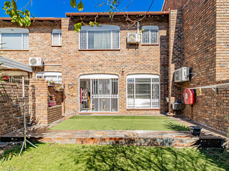 Rear exterior view of a face brick apartment featuring a tiled patio area, artificial lawn, and secure sliding door access.