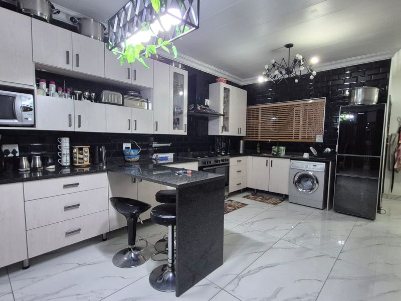 Modern kitchen featuring granite countertops, subway tile backsplash, built-in cabinetry, gas hob, and integrated laundry facilities in a spacious open-plan layout.