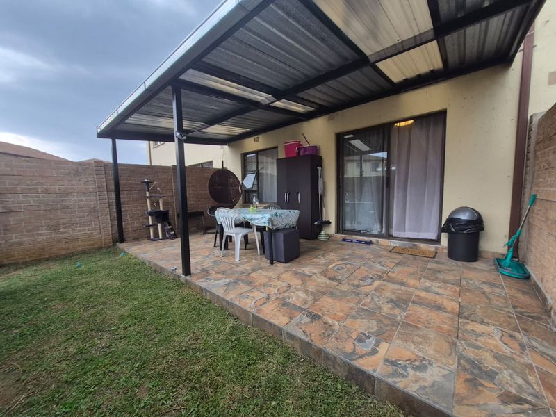 A covered outdoor patio area featuring tiled flooring and direct access to the interior through sliding glass doors, enclosed by a brick boundary wall.