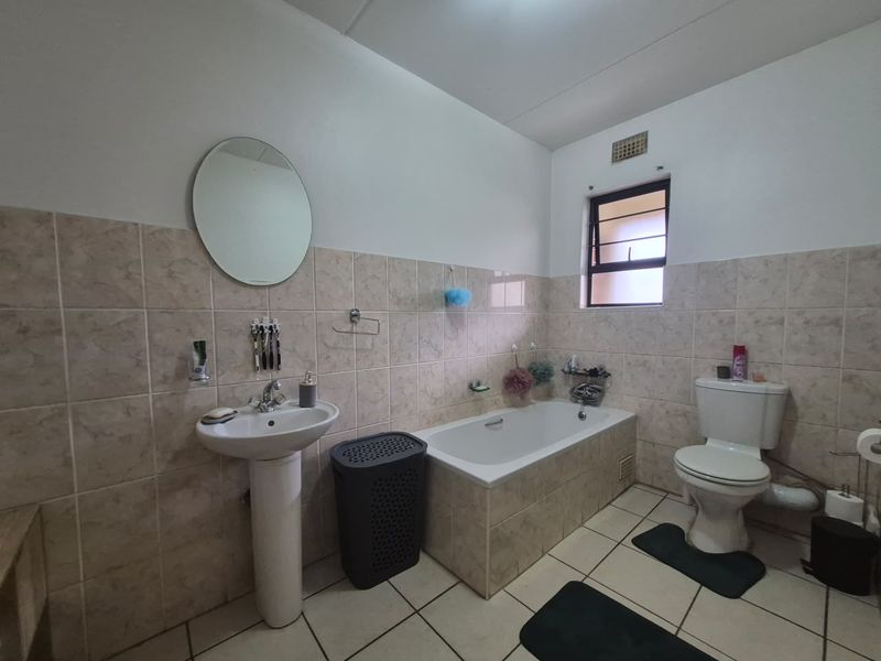 A functional bathroom featuring a pedestal basin, built-in bathtub, and toilet with neutral wall and floor tiling.