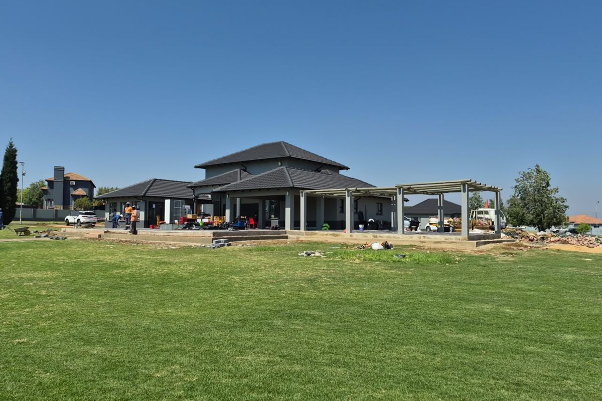 Rear view of a residential property under construction, featuring a large lawn, concrete patio area, and an installed pergola structure.