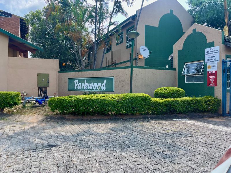Front entrance view of Parkwood complex featuring paved driveway, perimeter wall with electric fencing, and established garden landscaping.