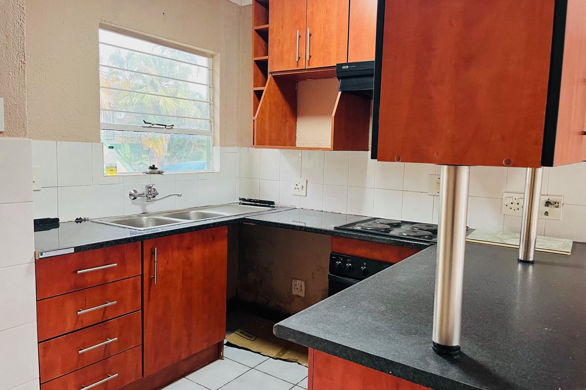 A functional kitchen featuring dark granite countertops, wooden cabinetry, and a double basin sink, requiring minor cosmetic updates to the wall finishes.