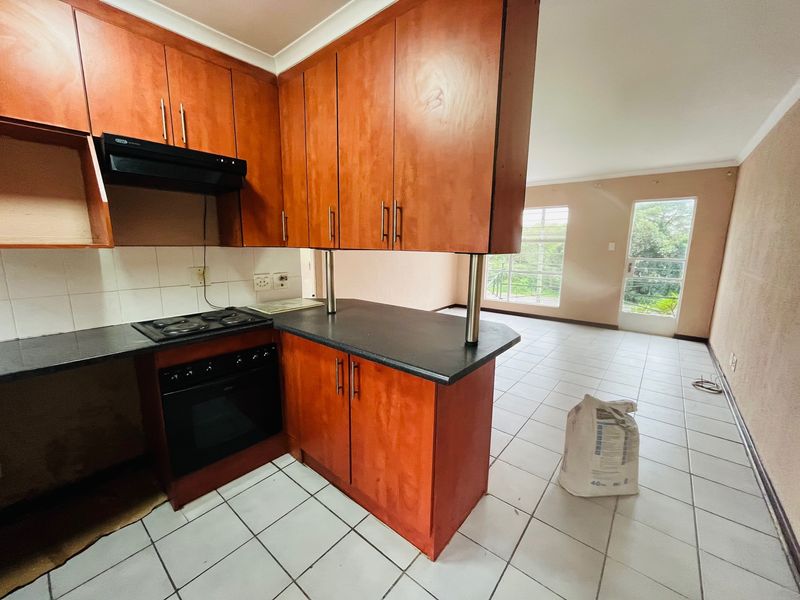 Open-plan kitchen and living area featuring wooden cabinetry, built-in appliances, and tiled flooring, offering a functional layout with natural light.