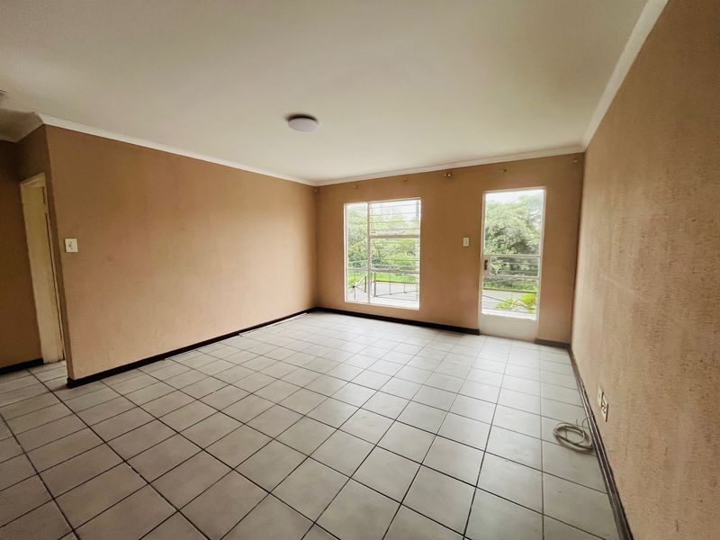 An empty living room featuring neutral wall paint, tiled flooring, and natural light through a window and glass door.