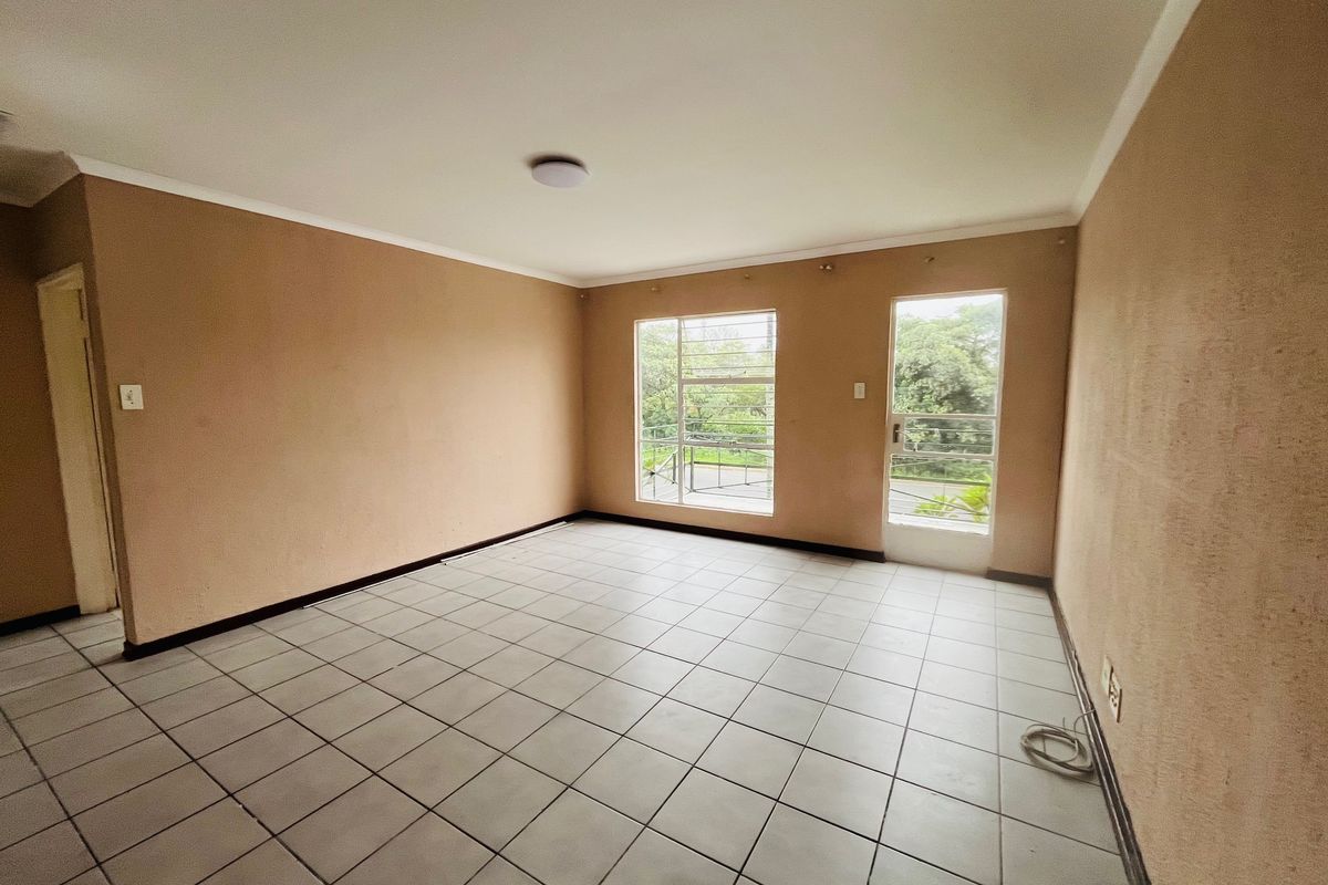 An empty living room featuring neutral wall paint, tiled flooring, and natural light through a window and glass door.