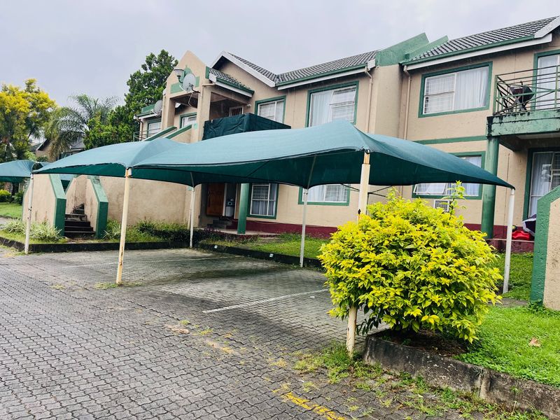 Front exterior view of an apartment complex featuring a paved driveway with shade cloth carports and multi-level residential units.