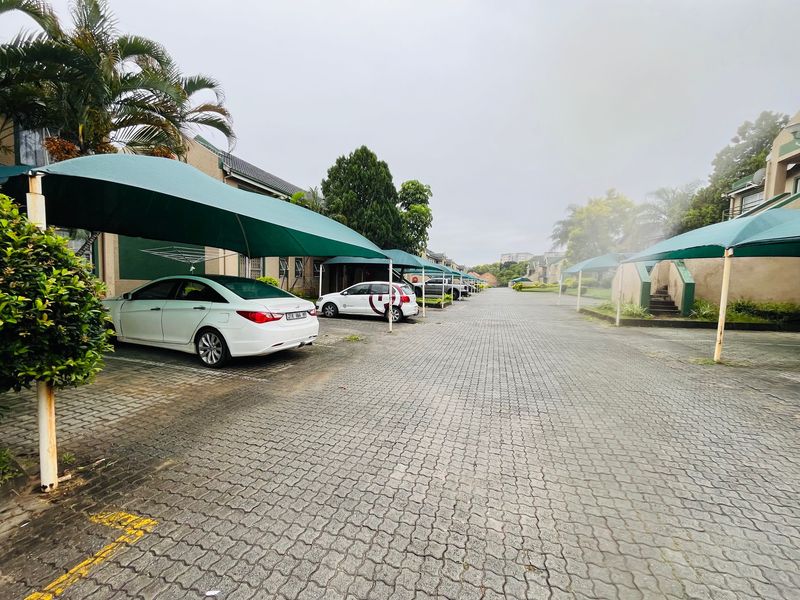 Exterior view of the apartment complex parking area featuring paved driveways and multiple shade cloth carports for resident vehicle protection.