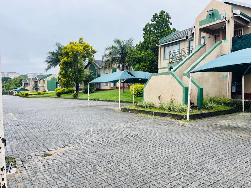 Exterior view of an apartment complex featuring a paved driveway, covered parking bays, and external staircases leading to upper-level units.