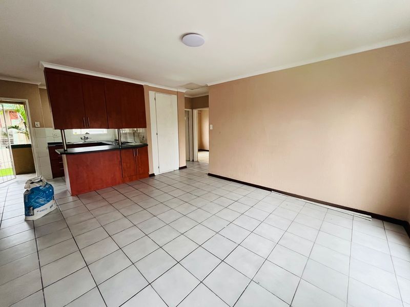 An open-plan living and kitchen area featuring tiled flooring, built-in wooden cabinetry, and neutral wall tones, offering a blank canvas for interior design.