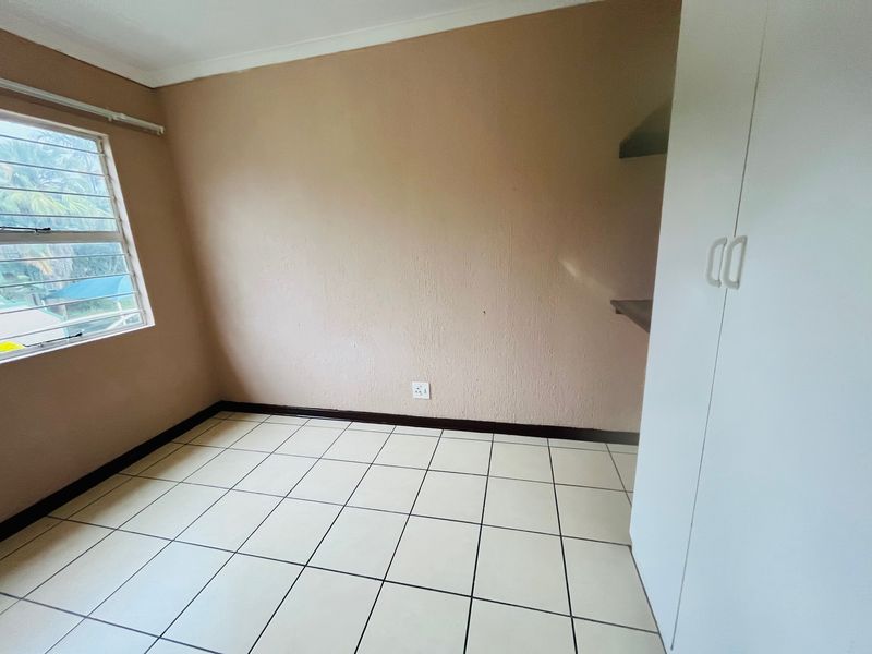 An empty bedroom featuring tiled flooring, a built-in cupboard, and a window with security bars, offering a blank canvas for personalization.