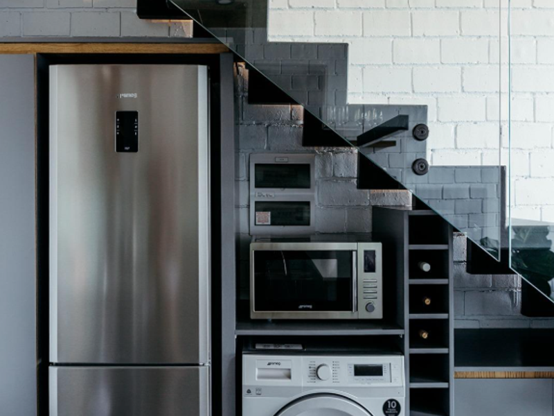 Modern kitchen area featuring integrated appliances, custom cabinetry, and a wine rack, cleverly designed beneath a contemporary glass and metal staircase.