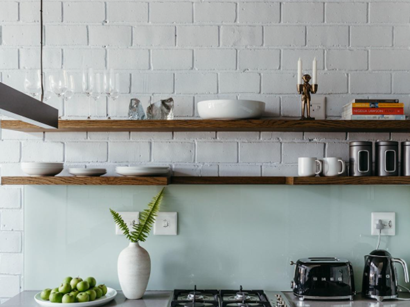 Modern kitchen featuring a gas hob, built-in oven, stone countertops, glass splashback, and stylish exposed concrete ceiling with floating timber shelving.