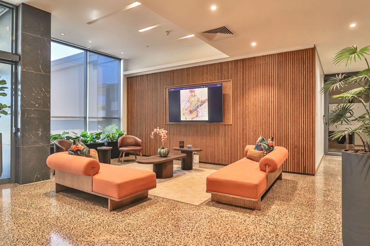 A modern, well-appointed lounge area featuring elegant timber slat wall paneling, polished terrazzo flooring, and floor-to-ceiling windows providing ample natural light.