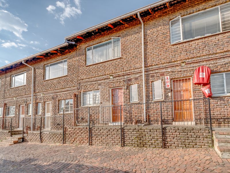 Front elevation of a multi-unit townhouse complex featuring exposed brick facade, paved driveway, and security-gated entrances.