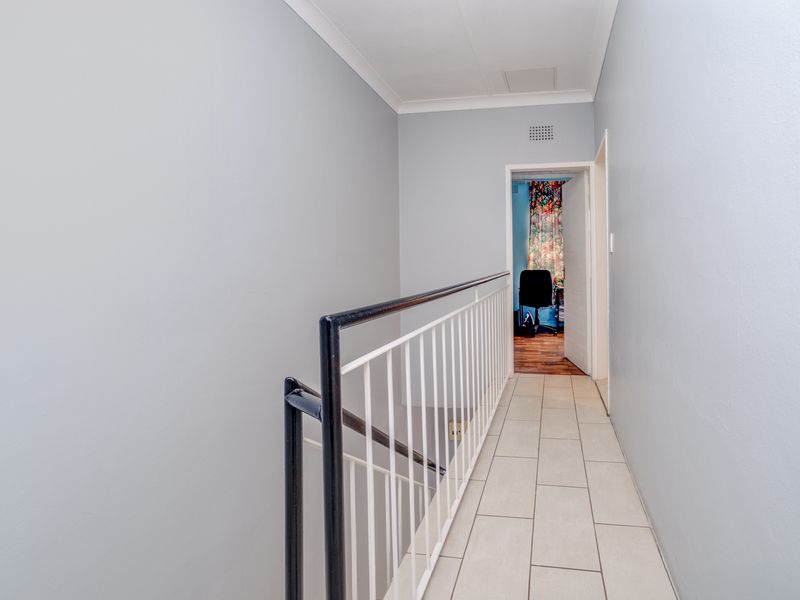 A clean and well-maintained upper-level hallway featuring tiled flooring and a secure metal balustrade overlooking the staircase.