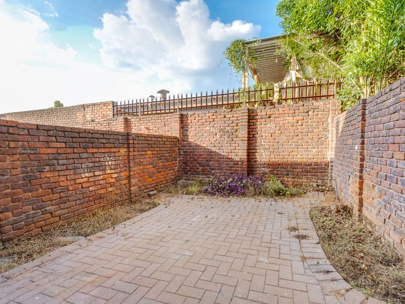 A private rear courtyard featuring a paved patio area enclosed by high brick boundary walls with security spikes.