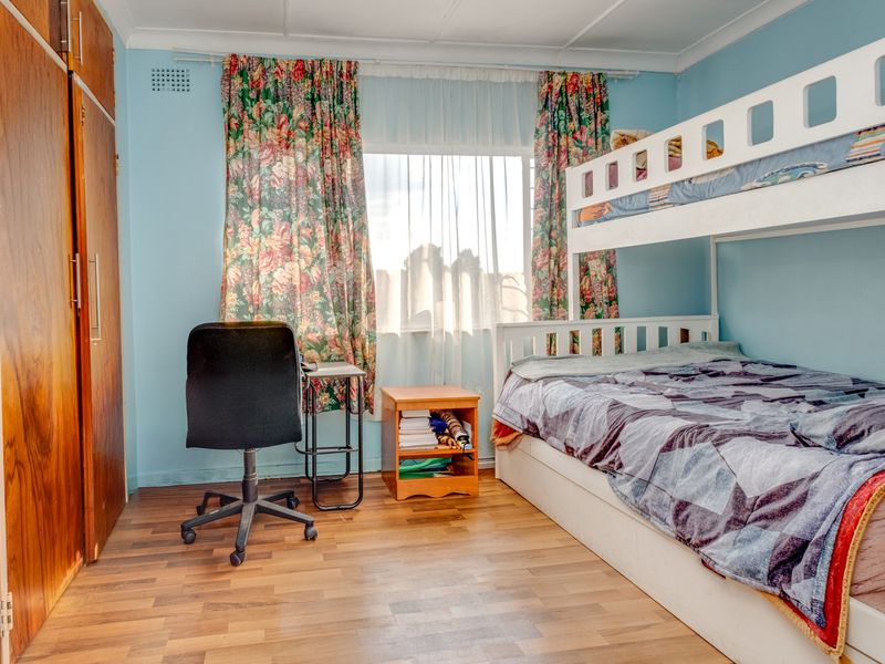 A functional bedroom featuring laminate flooring and a built-in wooden wardrobe, offering a practical layout with natural light from the window.