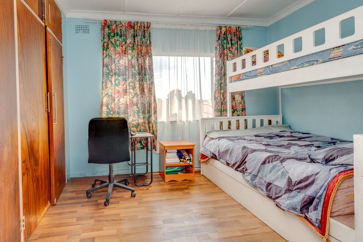 A functional bedroom featuring laminate flooring and a built-in wooden wardrobe, offering a practical layout with natural light from the window.