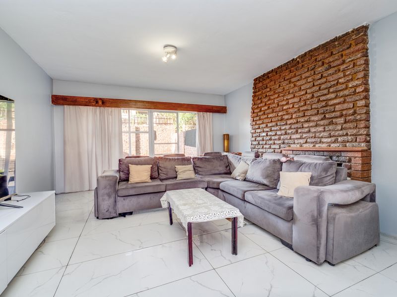 Spacious living room featuring a striking exposed brick feature wall, timber beam detail, and modern large-format marble-look floor tiles with access to the rear.