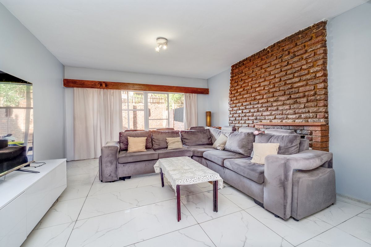 Spacious living room featuring a striking exposed brick feature wall, timber beam detail, and modern large-format marble-look floor tiles with access to the rear.