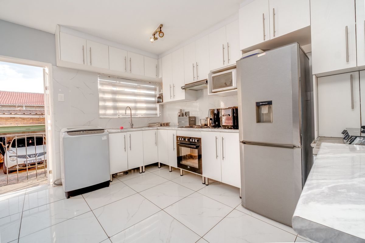 Modern kitchen featuring white cabinetry, marble-look countertops and wall tiles, built-in oven, hob, and extractor fan, with direct access to an outdoor area.