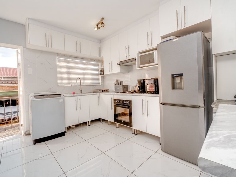 Modern kitchen featuring white cabinetry, marble-look countertops and wall tiles, built-in oven, hob, and extractor fan, with direct access to an outdoor area.