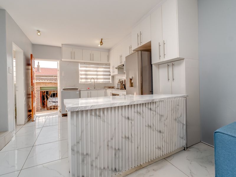 Modern kitchen featuring white cabinetry, a marble-look island, and tiled flooring, with direct access to the exterior.