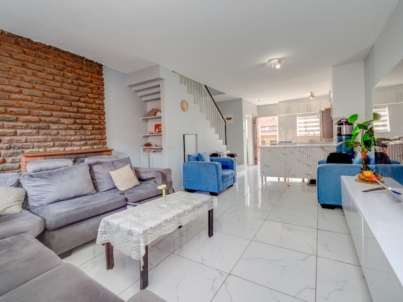 Spacious open-plan living and kitchen area featuring a striking exposed brick wall, modern marble-look floor tiles, and a functional kitchen island.