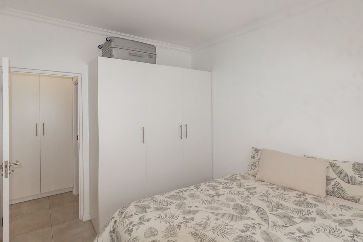 A clean and functional bedroom featuring built-in cupboards, neutral tiled flooring, and classic coving detail.