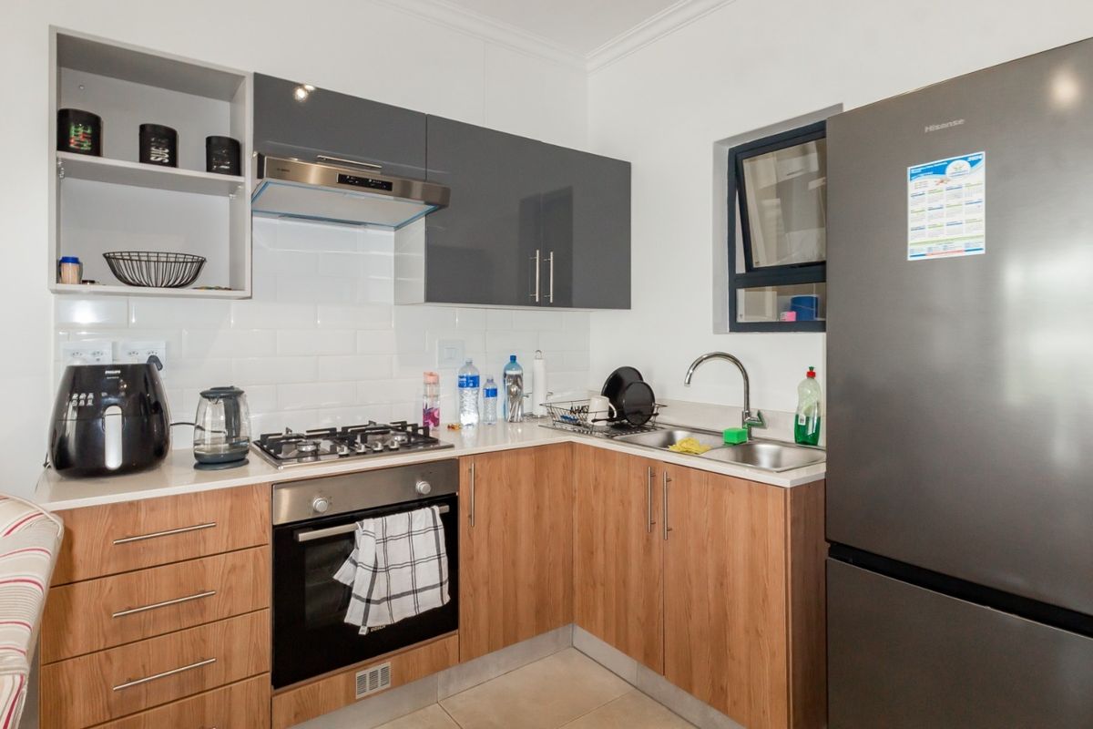 A modern, well-maintained kitchen featuring wood-finish cabinetry, grey overhead cupboards, a gas hob, built-in oven, and a clean tiled splashback.