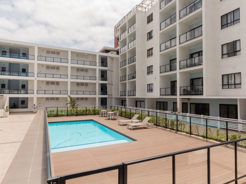 A well-maintained communal pool area featuring timber decking, glass balustrades, and tiled patio space within a modern apartment complex.