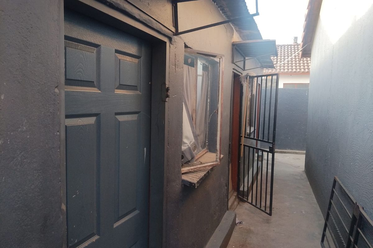 A narrow exterior side passage featuring a security gate, concrete pathway, and access to the rear of the property.